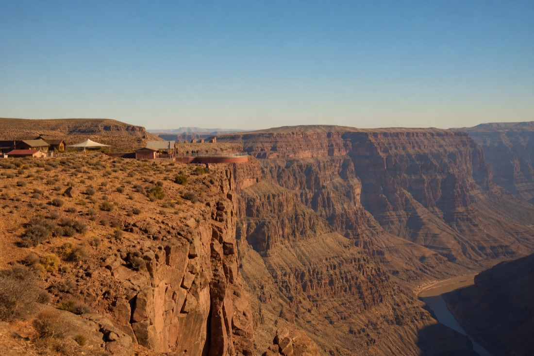 Visitors at a West Rim viewpoint at midday with sparse desert facilities behind them on Hualapai land