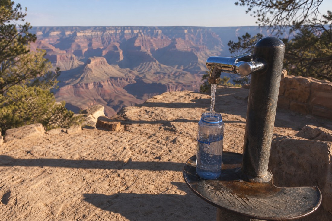 Refillable water bottle at a shaded refill station near a Grand Canyon rim path in summer heat