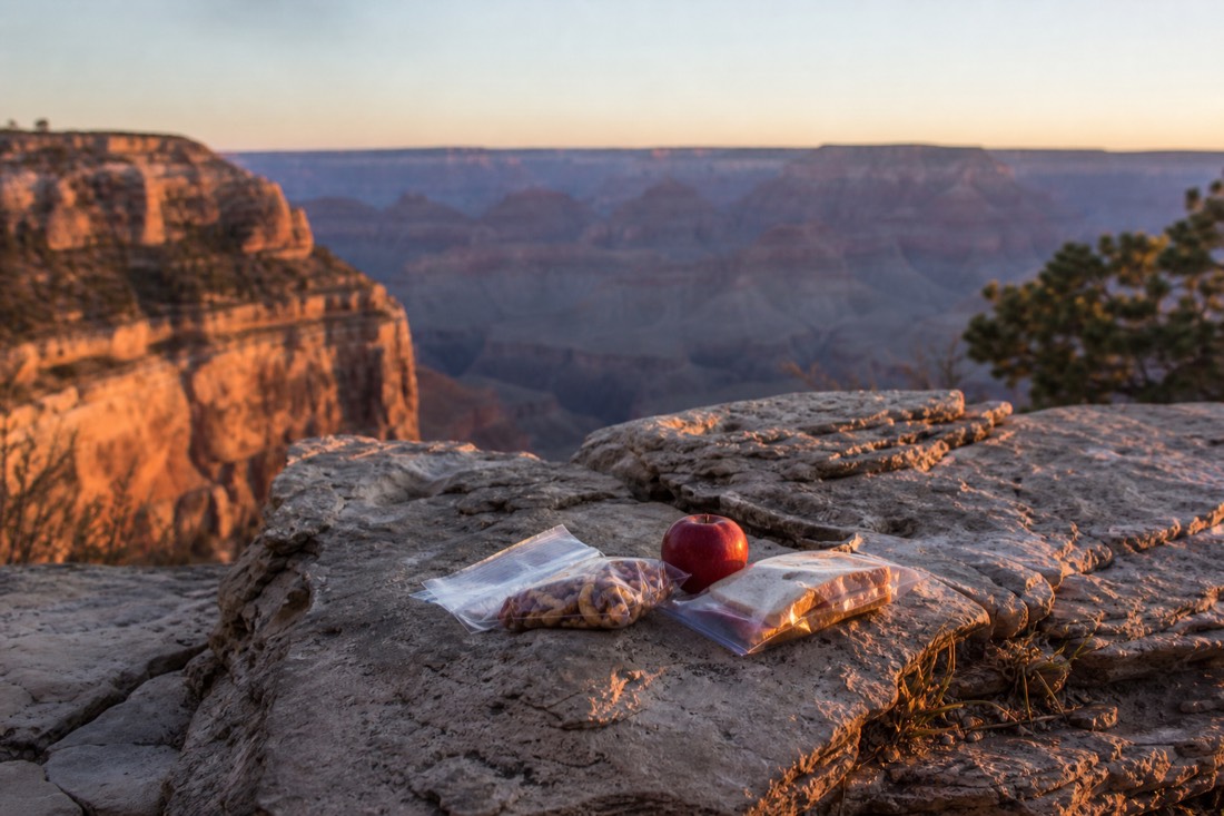 Picnic of simple trail food on a stone wall near a South Rim overlook in soft evening light