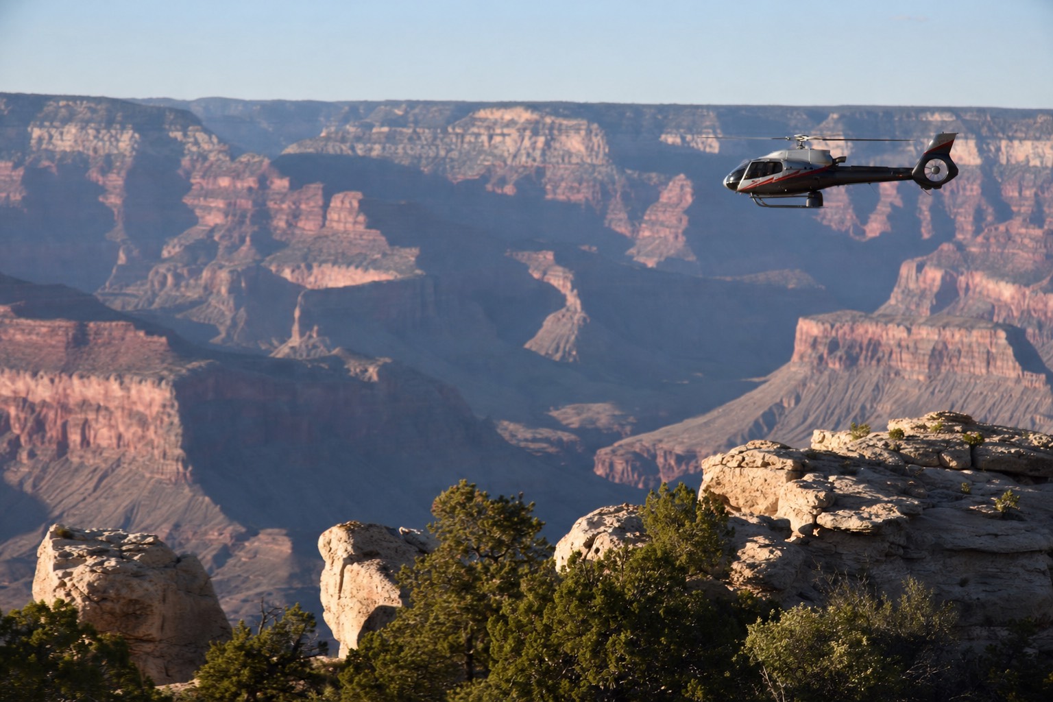 A tour helicopter crossing clear high-desert airspace near the Grand Canyon rim in morning light