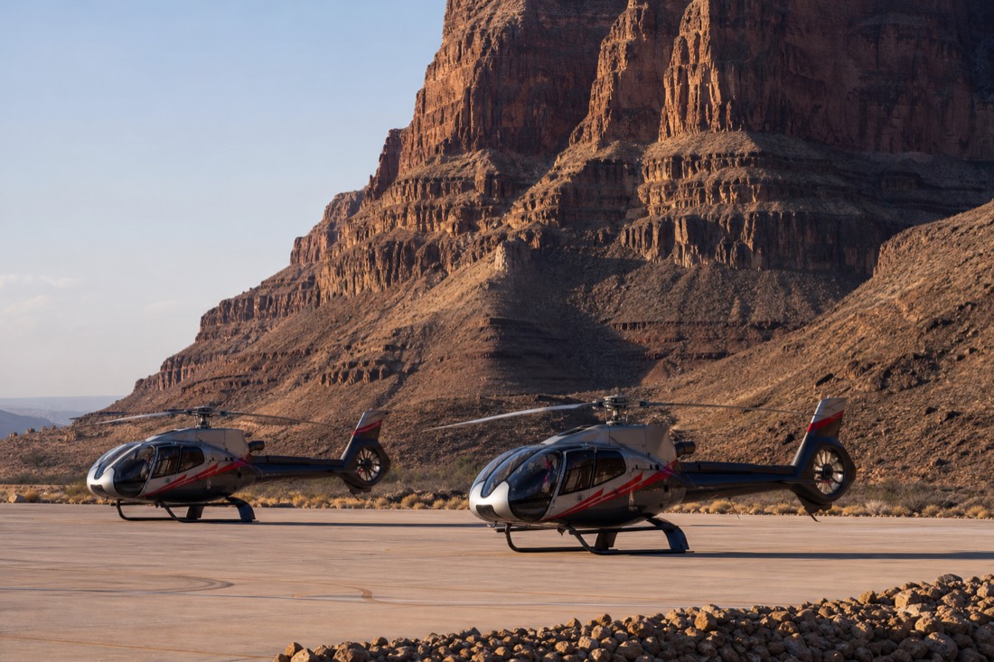 Two modern tour helicopters parked on a clean terminal apron in the desert