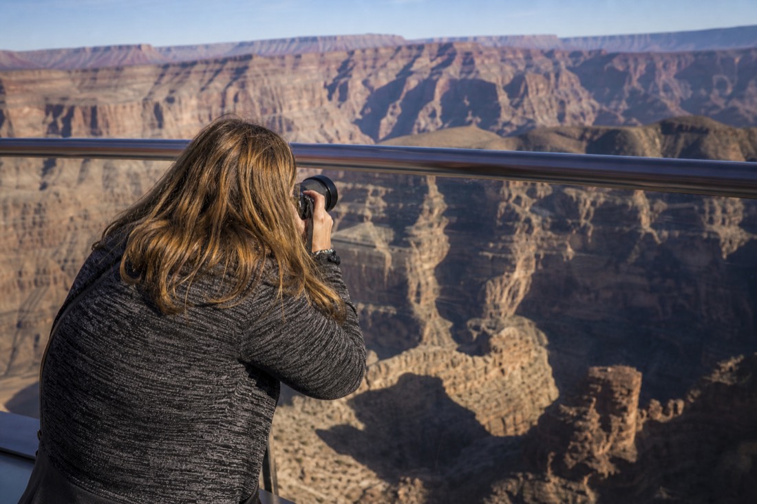 A visitor photographing the canyon through the glass rail of the Skywalk bridge at Grand Canyon West
