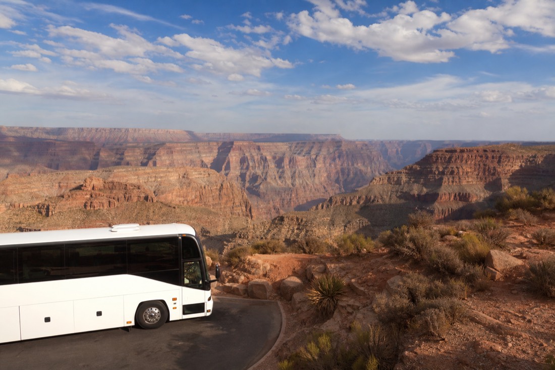 Tour coach parked at a West Rim overlook while visitors photograph the canyon at midday