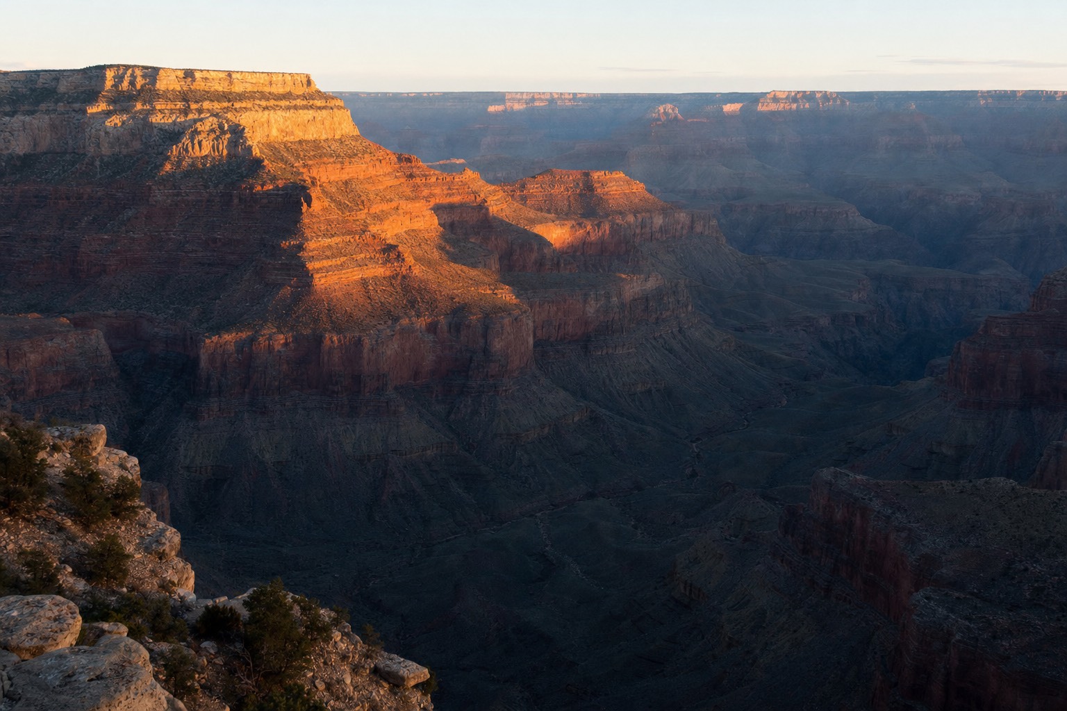 First light hitting the canyon walls below Mather Point on the Grand Canyon South Rim, buttes glowing orange above deep blue shadow