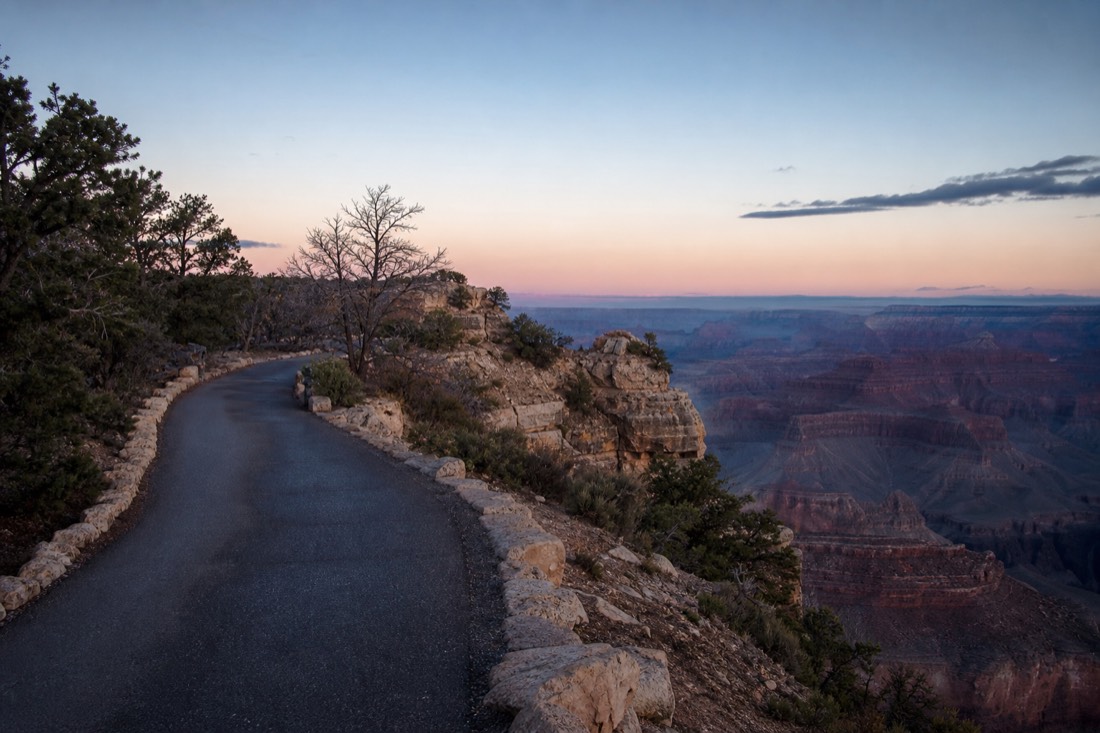 A paved rim path leading from the visitor center toward Mather Point in pre-dawn blue light