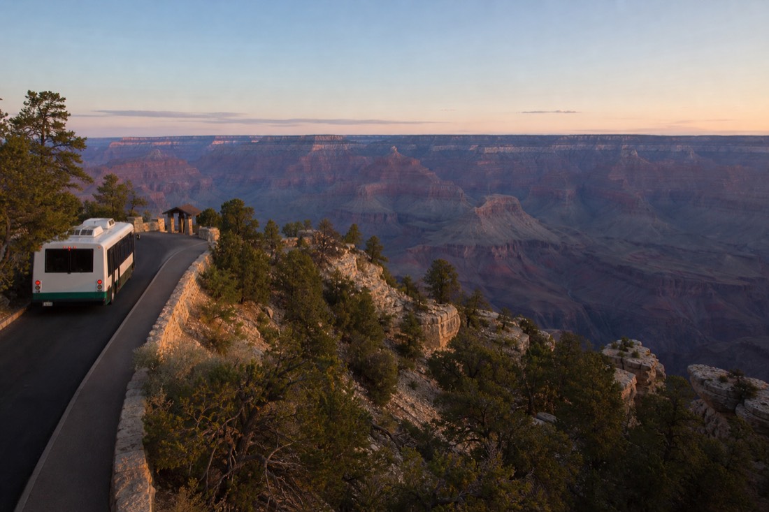 A park shuttle bus pulled up at a rim-side stop as visitors board in fading evening light