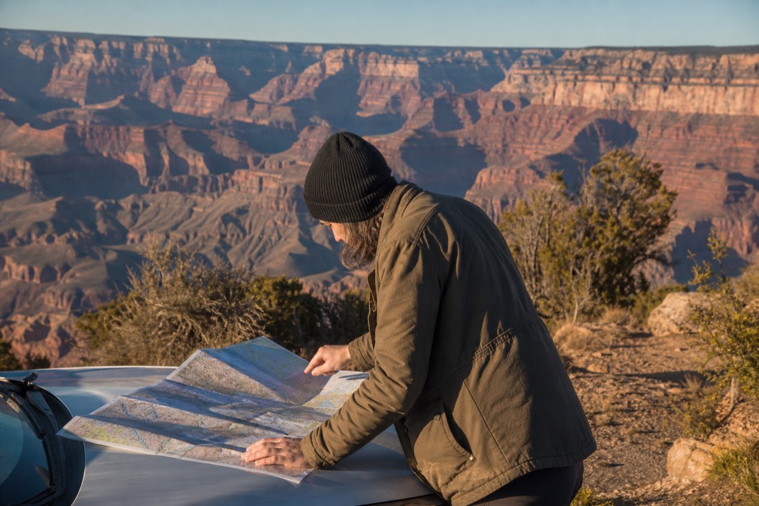 Traveler studying a paper road map on a car hood at a South Rim pullout with the canyon behind