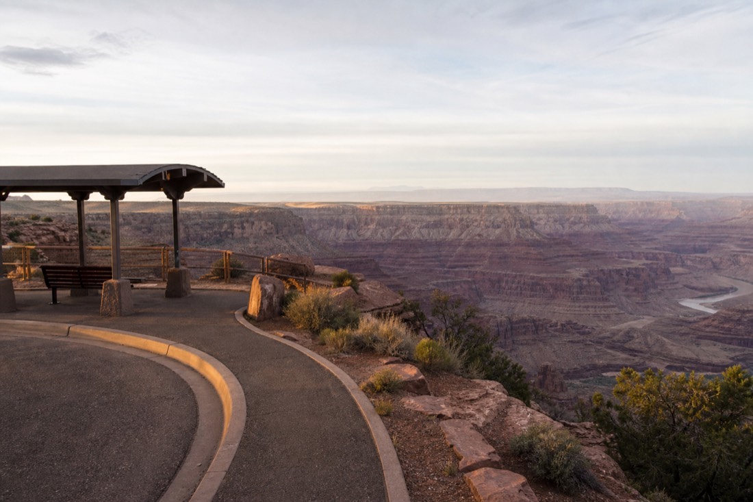 An open-air shuttle stop at a canyon rim viewpoint with red rock terraces dropping toward the Colorado River