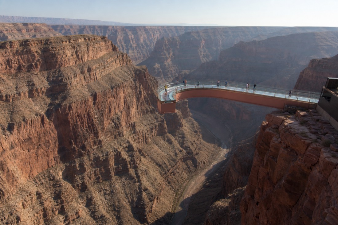 Visitors spaced out along a curved glass bridge over the canyon, small against the scale of the rock walls