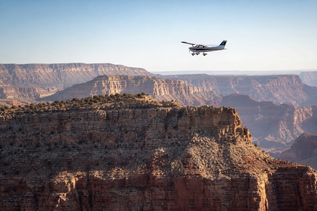 A small sightseeing aircraft holding a precise line over the canyon rim in clear morning air