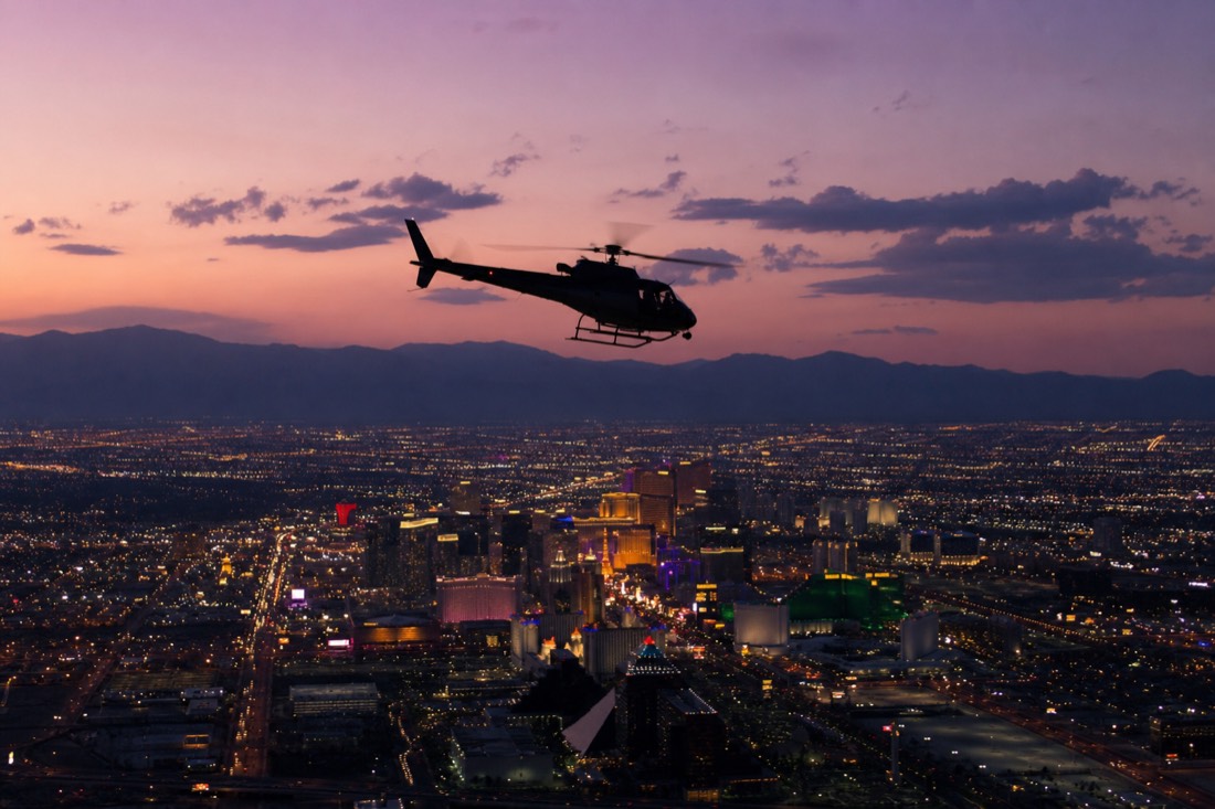 A helicopter flying toward the Las Vegas Strip at dusk with the city lights coming on