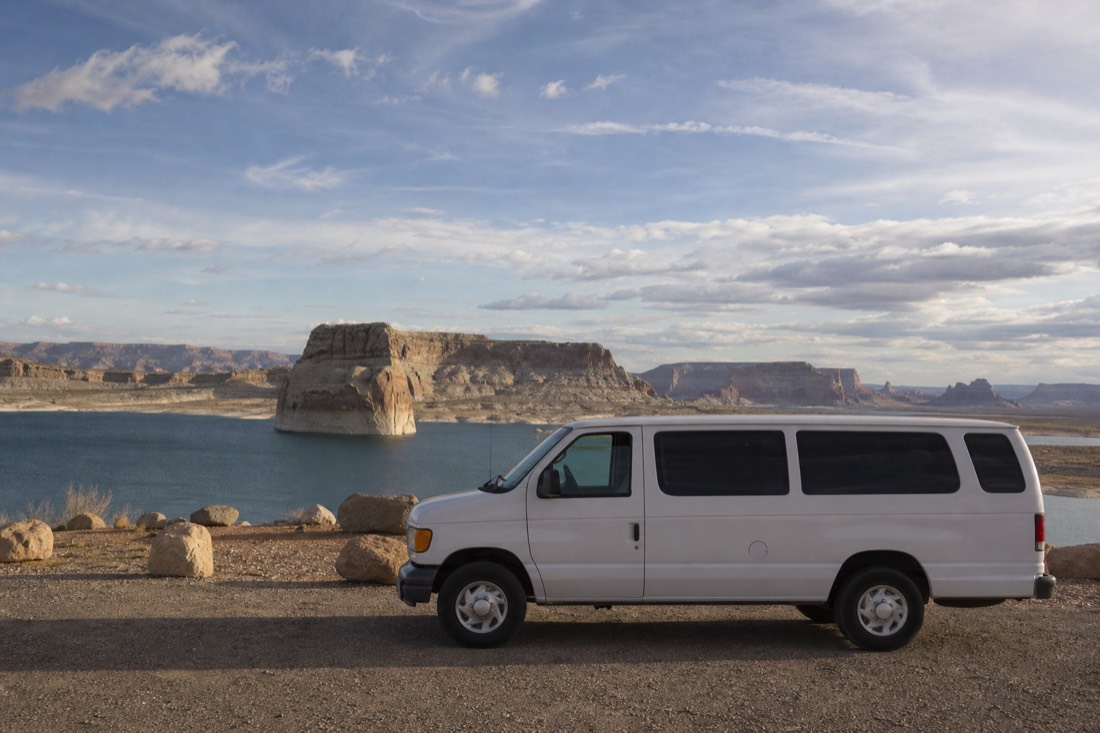 A small tour van parked at a Lake Powell overlook with red sandstone and blue water stretching behind it