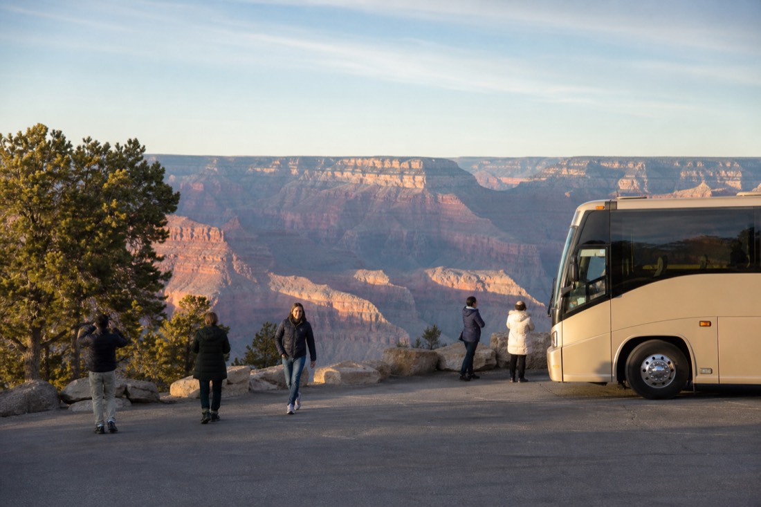 A modern tour coach parked near the Grand Canyon rim while passengers step out with cameras