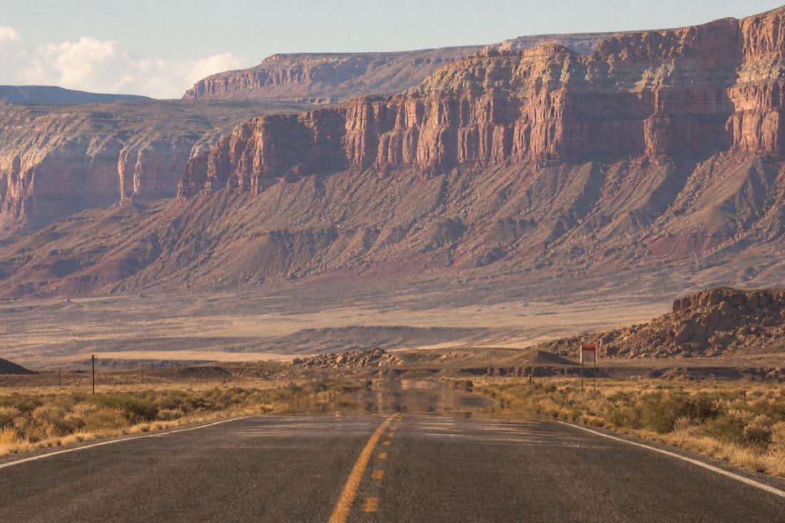 A two-lane desert road with heat shimmer rising and a lone gas station sign in the distance