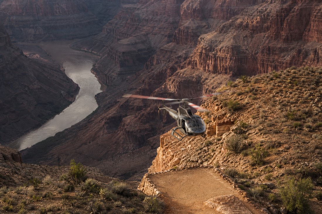 A sightseeing helicopter descending toward a landing terrace inside the Grand Canyon near the Colorado River