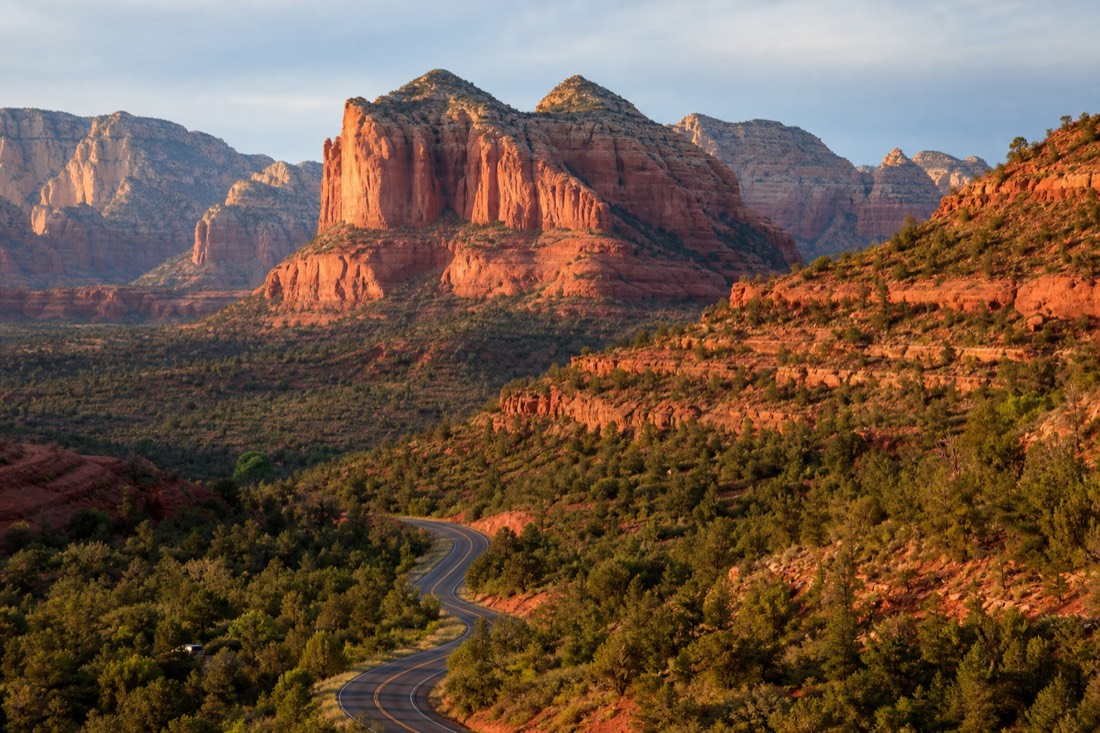 Red rock formations of Sedona glowing under morning light with the winding 89A road below