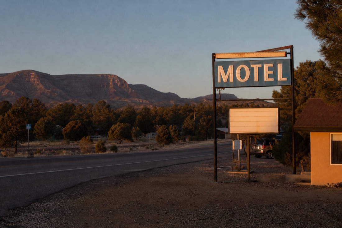 A warm-lit motel sign on Route 66 in Williams Arizona at dusk with pine trees behind