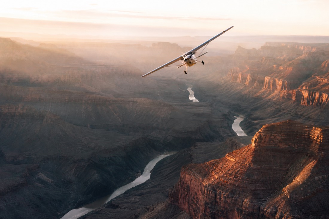 A small sightseeing airplane banking over the Grand Canyon with the Colorado River visible far below
