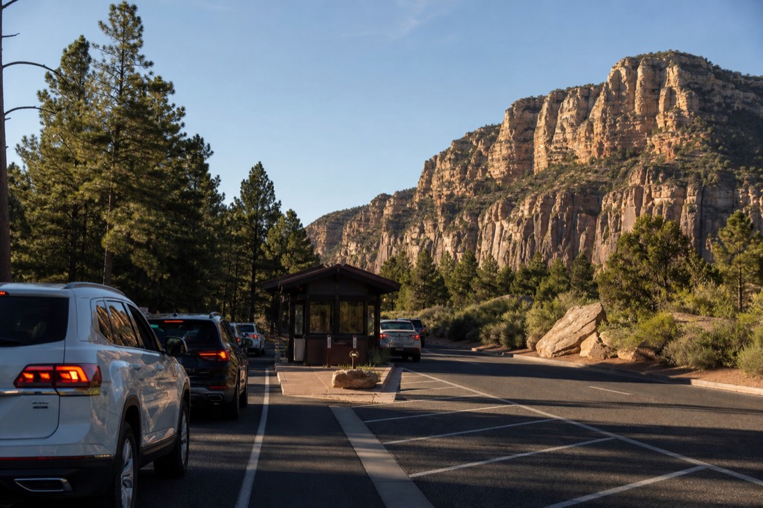 Cars queued at the Grand Canyon South Rim entrance station booth on a bright morning with pine forest behind