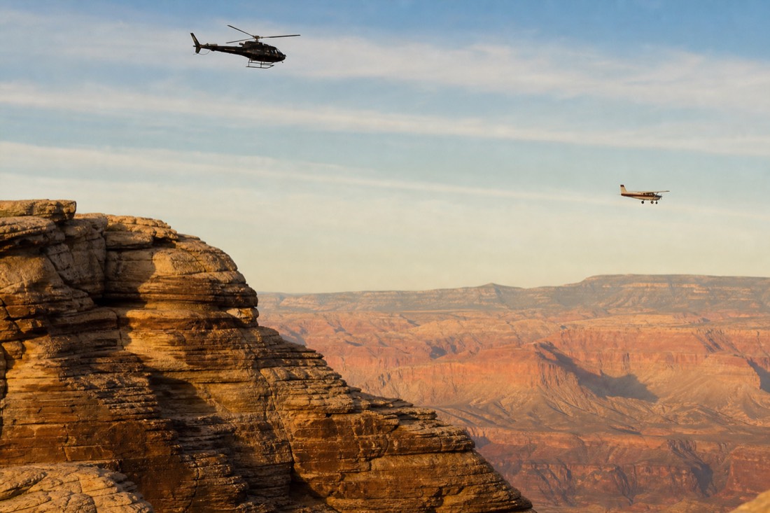 A helicopter and a small fixed-wing airplane crossing the same desert sky at different altitudes