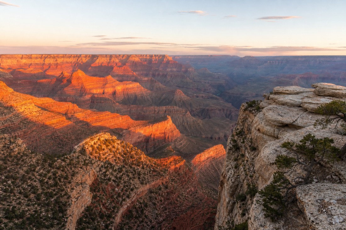 First light flooding the Grand Canyon with pink and gold as seen from a South Rim overlook before the crowds arrive