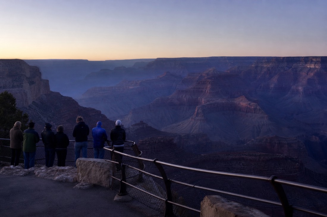 A handful of early risers wrapped in jackets waiting at the Mather Point railing in pre-dawn blue light