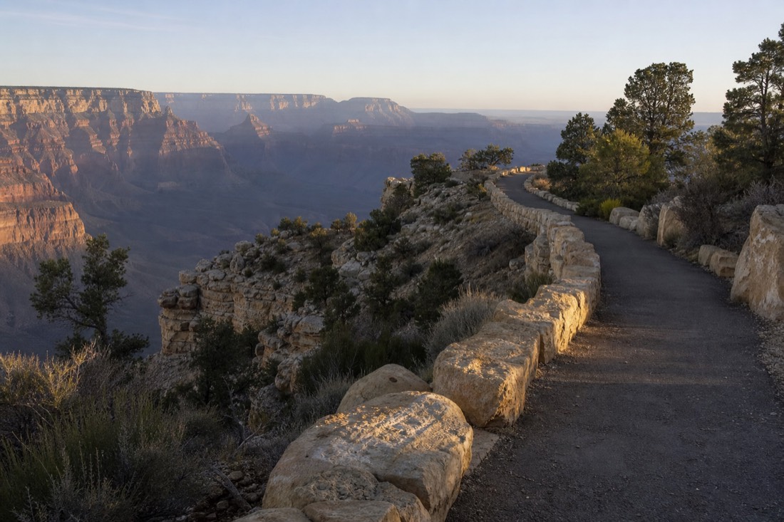 A walker on the paved Rim Trail with the canyon opening to the north and morning shadows still deep in the gorge