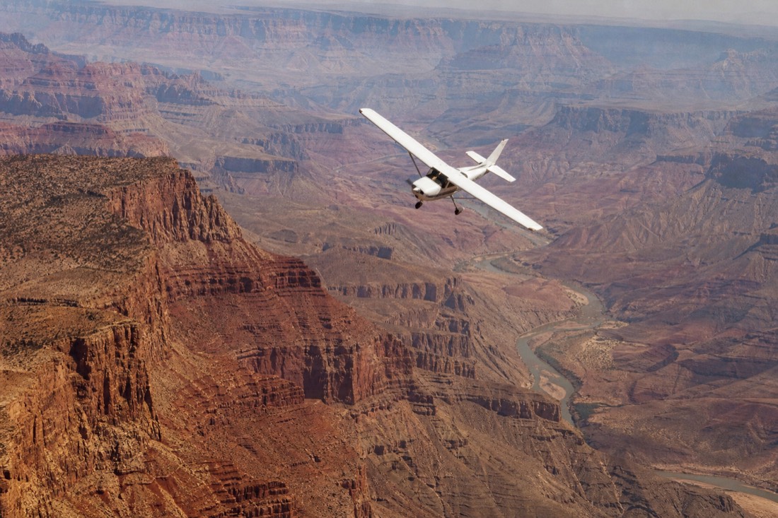 A small sightseeing airplane banking over the vast layered expanse of the Grand Canyon at midday