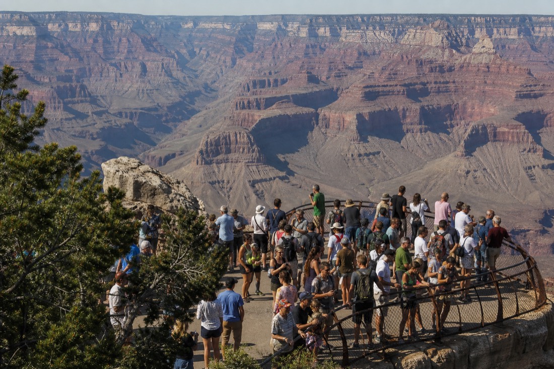 Crowd of visitors at the Mather Point railing at midday with the vast layered canyon stretching to the North Rim