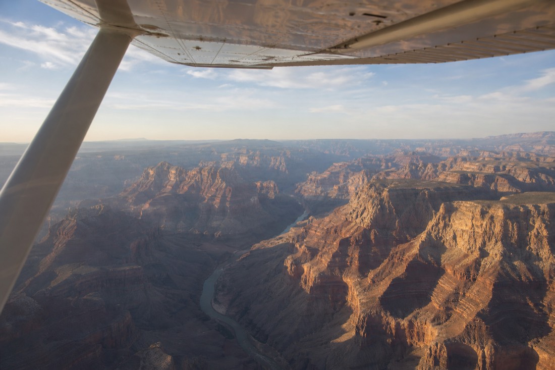 Wing-window view from a small aircraft over the Grand Canyon with the river threading between mesas far below