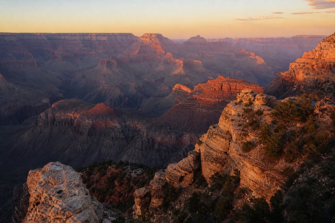Late afternoon light setting canyon buttes glowing orange and purple in deep haze from a South Rim overlook