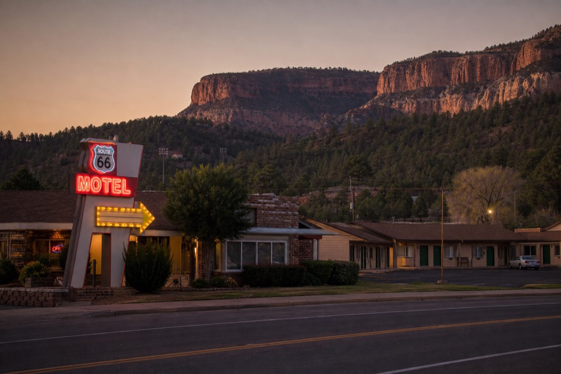 Route 66 motel neon glowing at dusk on the main street of Williams, Arizona with pine hills behind
